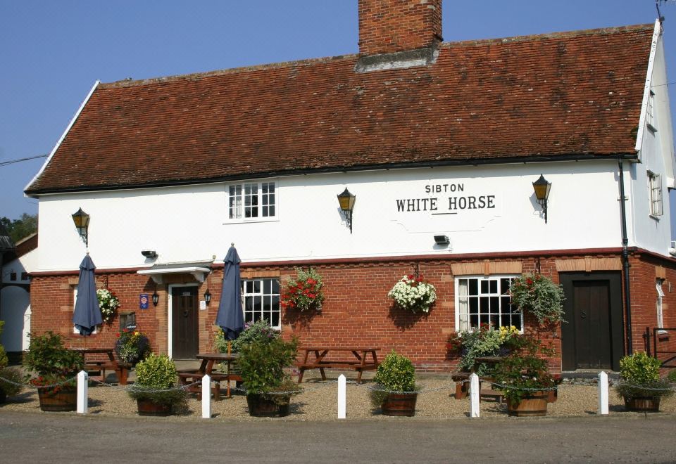 the white horse pub in essex , england , with its red brick and white exterior , surrounded by greenery and blue umbrellas at Sibton White Horse Inn