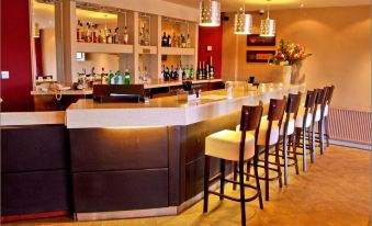a well - equipped bar with several stools and a long counter filled with bottles of liquor at Mode Hotel St Annes