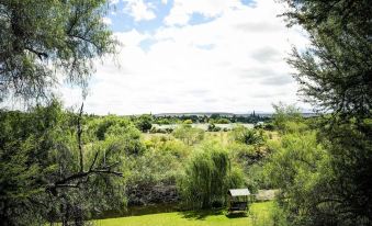 a beautiful landscape with trees , grass , and a wooden structure , as well as a grassy field under a blue sky at Riverside Guest Lodge