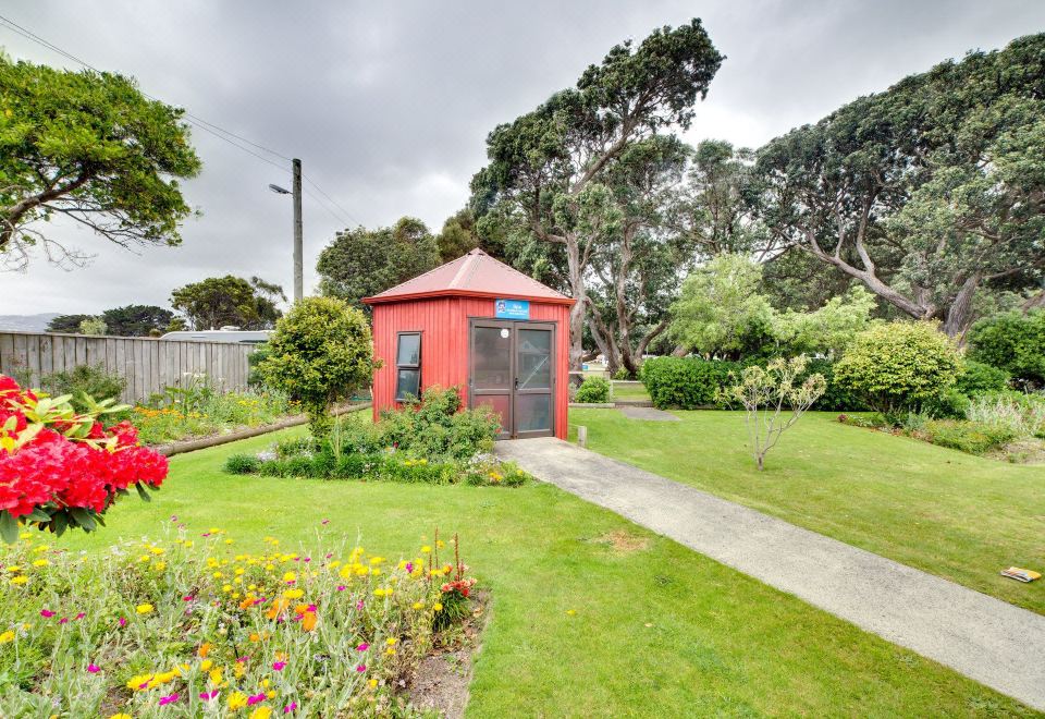 a small red shed with a window and a sign in front of it , surrounded by greenery and flowers at Wellington Top 10 Holiday Park