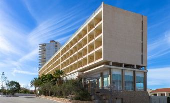 a large , beige - colored building with a row of windows and balconies is situated on a street next to a modern high - rise at Hotel Dos Playas