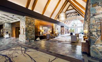 a spacious lobby with high ceilings , stone walls , and wooden beams , featuring a large floor - to - ceiling window and a stone fireplace at Fairmont Chateau Whistler