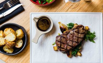 a dining table with a white plate containing a steak and vegetables , accompanied by a fork , knife , and wine at Novotel Sydney Darling Harbour