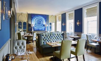 a modern , elegant restaurant with blue walls and wooden floors , featuring comfortable seating arrangements and a large abstract art piece on the wall at The Woburn