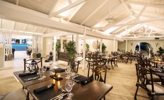 a large dining room with wooden floors , tables , chairs , and plants , as well as people sitting at the tables at Bougainvillea Barbados