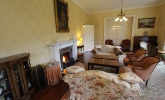 a cozy living room with a fireplace , two couches , and a painting on the wall at Glengarry Castle Hotel
