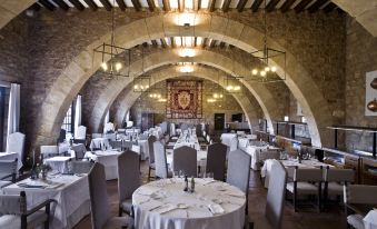 a large , empty restaurant with stone walls and arches , decorated with white tablecloths and elegant dining settings at Parador de Siguenza