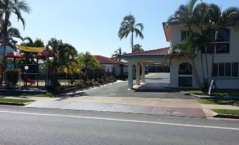 a driveway leading to a large house with palm trees and a clear blue sky at Tropic Coast Motel