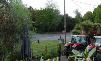 a garden with a tractor parked next to a fence , surrounded by green grass and trees at The Mortimer Arms