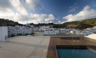 a rooftop pool surrounded by a wooden deck , with a view of the city in the background at Hotel Loar Ferreries