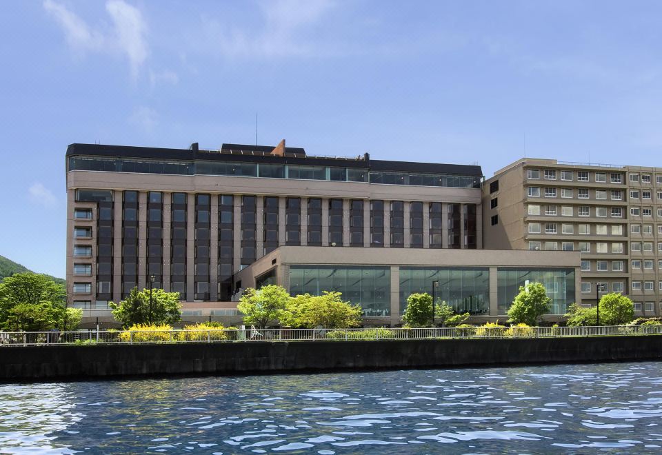 a large building with a flat roof and many windows is situated near the water at The Lake View Toya Nonokaze Resort