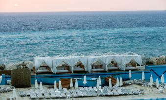 a large outdoor pool surrounded by white lounge chairs and umbrellas , with the ocean in the background at Four Seasons Halat