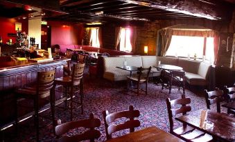a room with wooden furniture and a bar area featuring white walls and red brick ceiling at The Anchor Inn