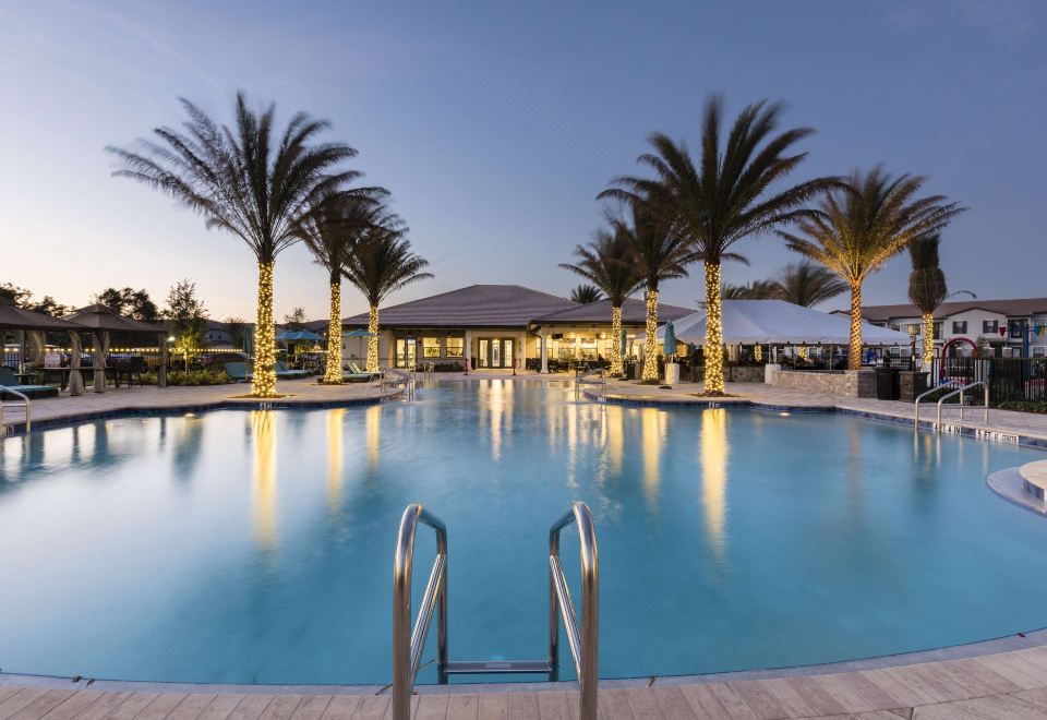 a large outdoor swimming pool surrounded by palm trees , with people enjoying their time in the water at Balmoral Resort Florida