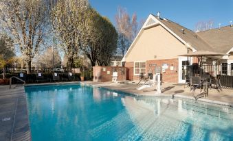 a large outdoor swimming pool surrounded by a brick building , with several lounge chairs and umbrellas placed around the pool area at Residence Inn Stockton