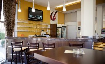 a modern restaurant with a yellow wall , black chairs , and a counter , where people are seated and enjoying their meals at Hotel Grand