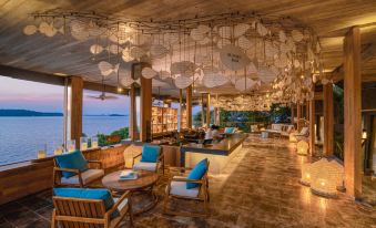 a large , modern restaurant with wooden furniture and a view of the ocean is decorated with hanging lanterns at Six Senses Krabey Island