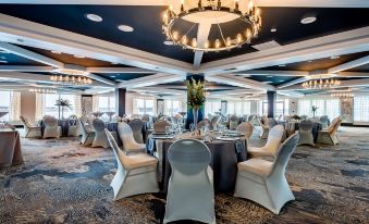 a large , empty banquet hall with multiple round tables set for a formal event , surrounded by chairs and chandeliers at Holiday Inn Grand Haven-Spring Lake