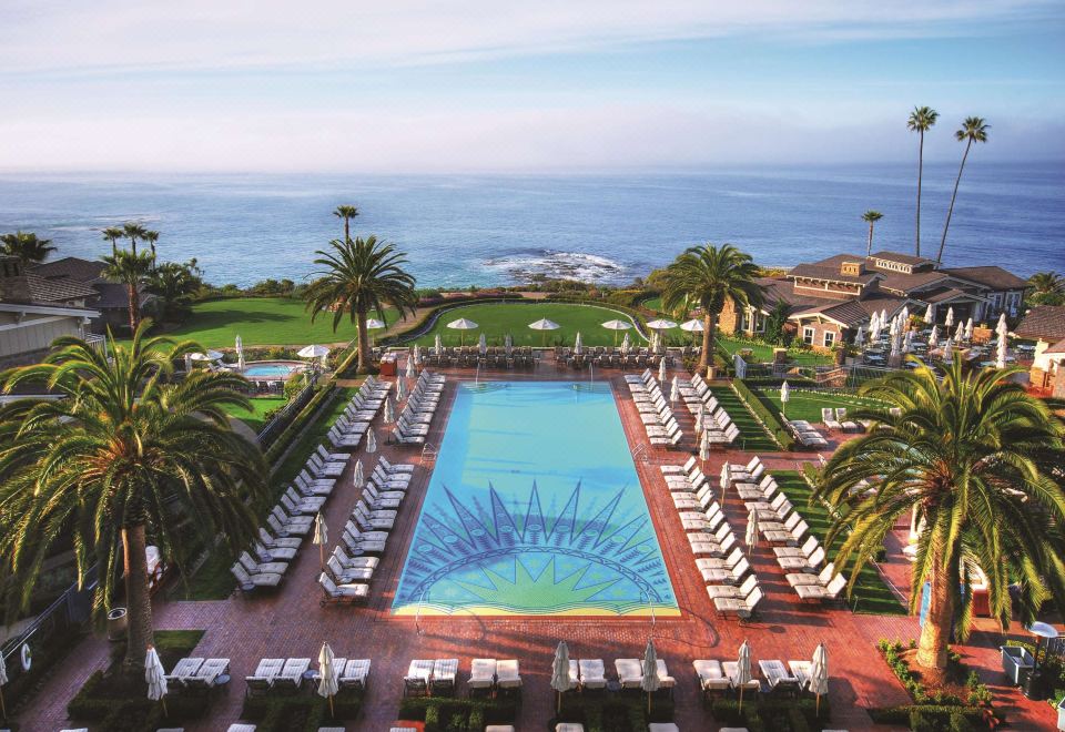 a large swimming pool surrounded by lounge chairs and palm trees , with the ocean in the background at Montage Laguna Beach