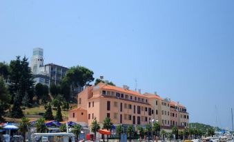 a large building with a red roof is situated next to a marina filled with boats at Maistra Select Riva Apartments