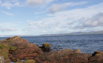 a rocky shoreline near a body of water , with the sky filled with clouds and water covering the surface at Kennels