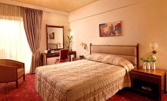 a large bed with a wooden headboard and beige bedding is in a room with a desk , chair , and window at Savoy Hotel