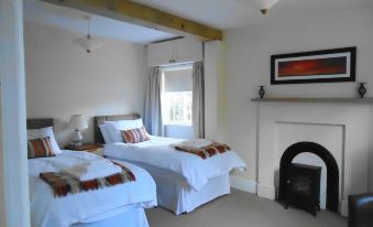 a bedroom with two beds , a fireplace , and a painting on the wall , giving it a cozy and inviting atmosphere at The Old Post House