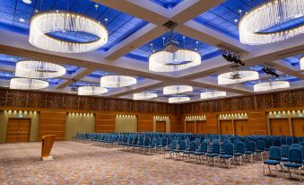 a large , empty conference room with wooden walls and high ceilings , featuring rows of blue and white chairs arranged in an auditorium - like setting at Radisson Blu M'Bamou Palace Hotel, Brazzaville