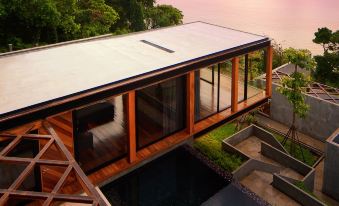 a modern house with a large glass window overlooking a pool , surrounded by lush greenery at The Naka Phuket, a member of Design Hotels