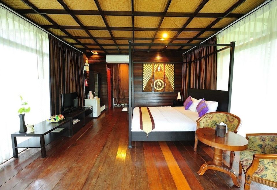 a cozy bedroom with hardwood floors , a large bed , and a tv . a wooden coffee table in the room at Suan Muang Porn