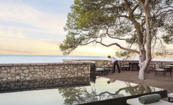 a person is sitting on a stone ledge overlooking the ocean with a tree in the background at Aman Sveti Stefan