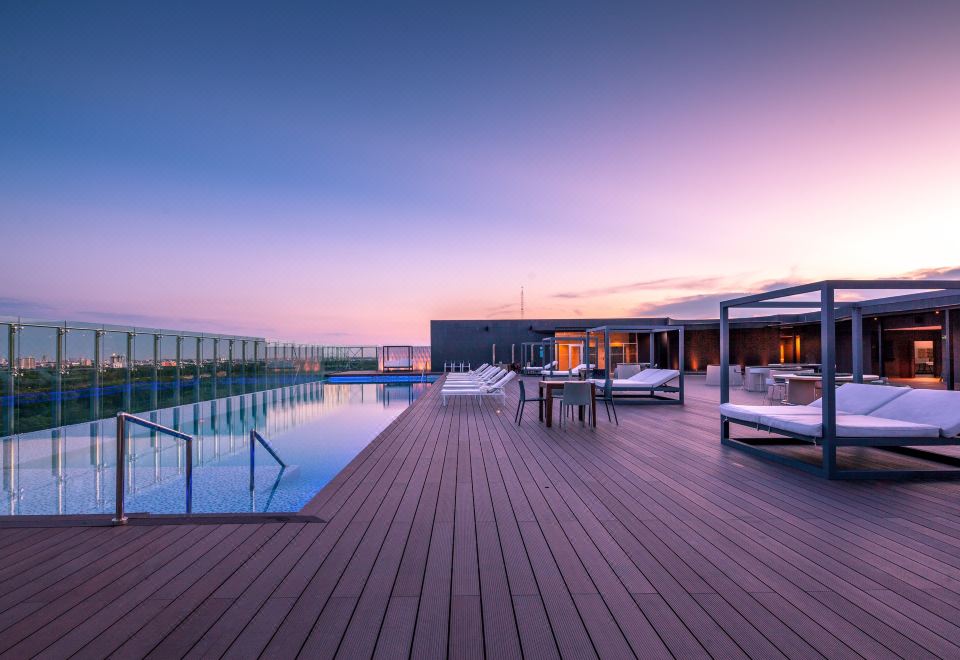 a rooftop pool surrounded by lounge chairs and a building , with the sun setting in the background at Radisson Hotel Santa Cruz