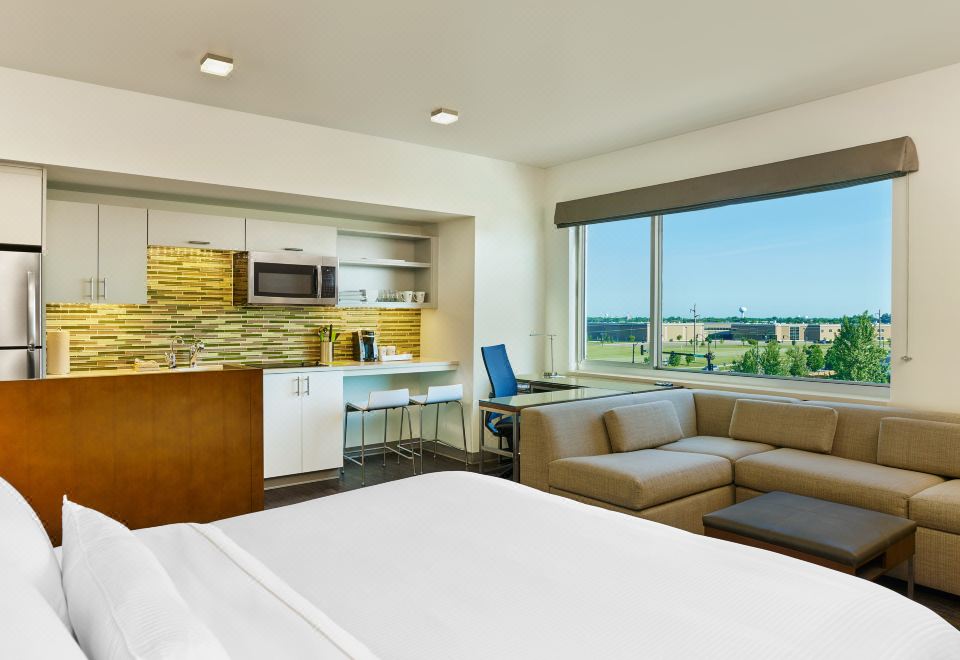 a modern hotel room with a large window overlooking a beautiful landscape , featuring a bed , couch , dining table , and kitchenette at Element Fargo