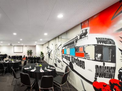 a large room with tables and chairs , a red train mural on the wall , and potted plants at Ibis Melbourne Hotel and Apartments