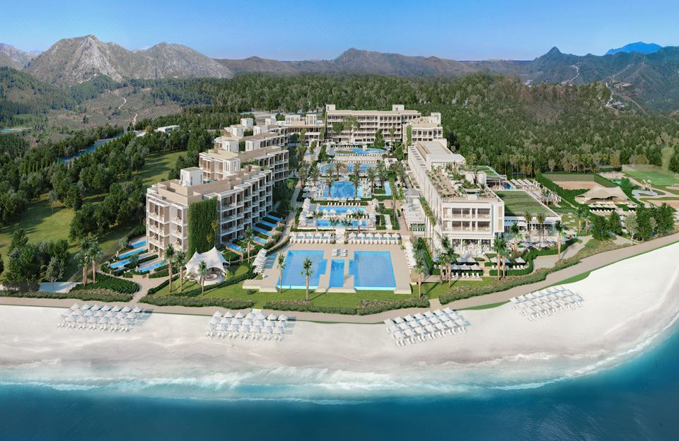a large resort with multiple swimming pools and buildings , surrounded by trees and mountains , on a beach at Ikos Andalusia