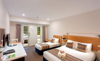 a hotel room with two beds , a desk , and an open door leading to a balcony at Berrima Bakehouse Motel