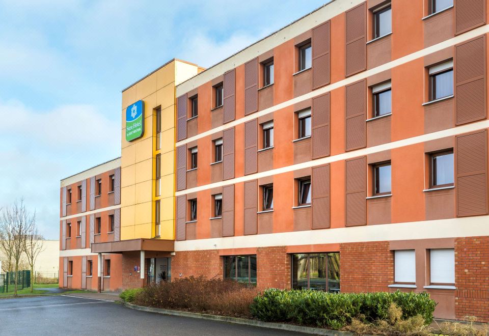 a modern hotel building with multiple floors , large windows , and a green logo on the sign at Sure Hotel by Best Western St-Amand-Les-Eaux
