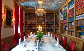 a dining room with a long table set for a formal dinner , surrounded by books and chandeliers at Haringe Slott