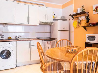 a kitchen with white cabinets , a wooden table and chairs , and a yellow wall hanging at Lanzarote