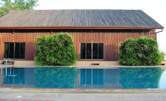 a large swimming pool is surrounded by a brick patio and a wooden building with shutters at Baan Thai Resort