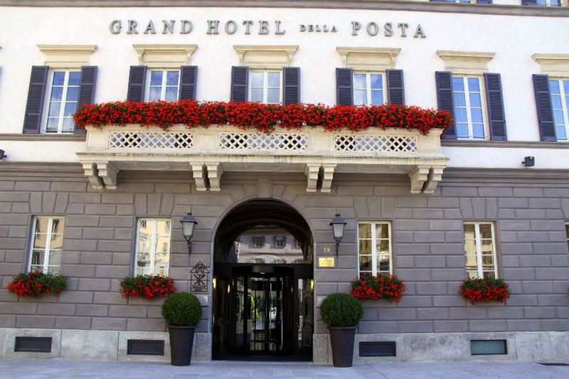 the grand hotel della posta is a grand hotel with white walls , red flowers , and black shutters at Grand Hotel Della Posta