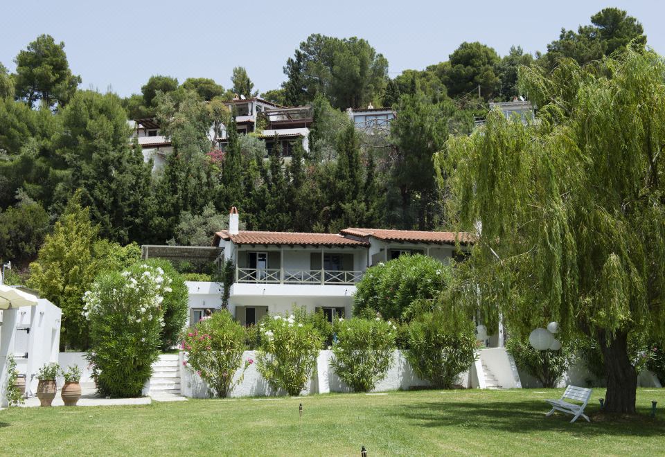 a large white house surrounded by trees and grass , with a fence surrounding the property at Skiathos Holidays Suites & Villas