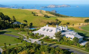 aerial view of a large white house surrounded by green fields , overlooking the ocean and mountains at Rosewood Kauri Cliffs