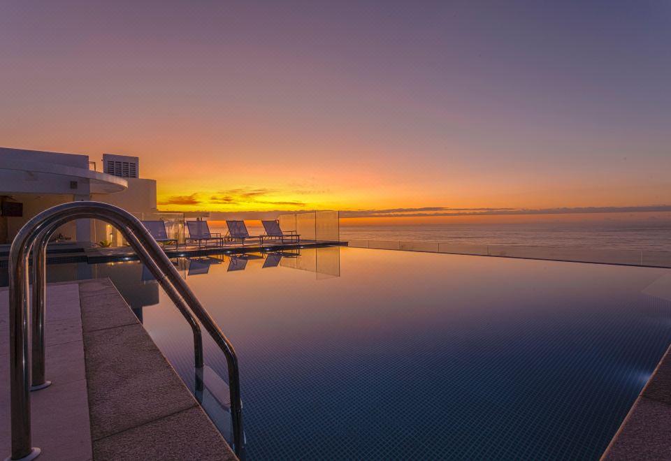 a large swimming pool with a sunset view , and several lounge chairs placed around it at CDesign Hotel