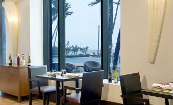 a restaurant with wooden tables and chairs , a bar area , and large windows overlooking the ocean at Novotel Mumbai Juhu Beach