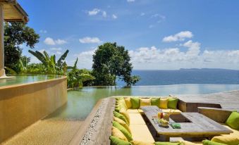 a large pool surrounded by lounge chairs and tables , with a view of the ocean in the background at Soneva Kiri