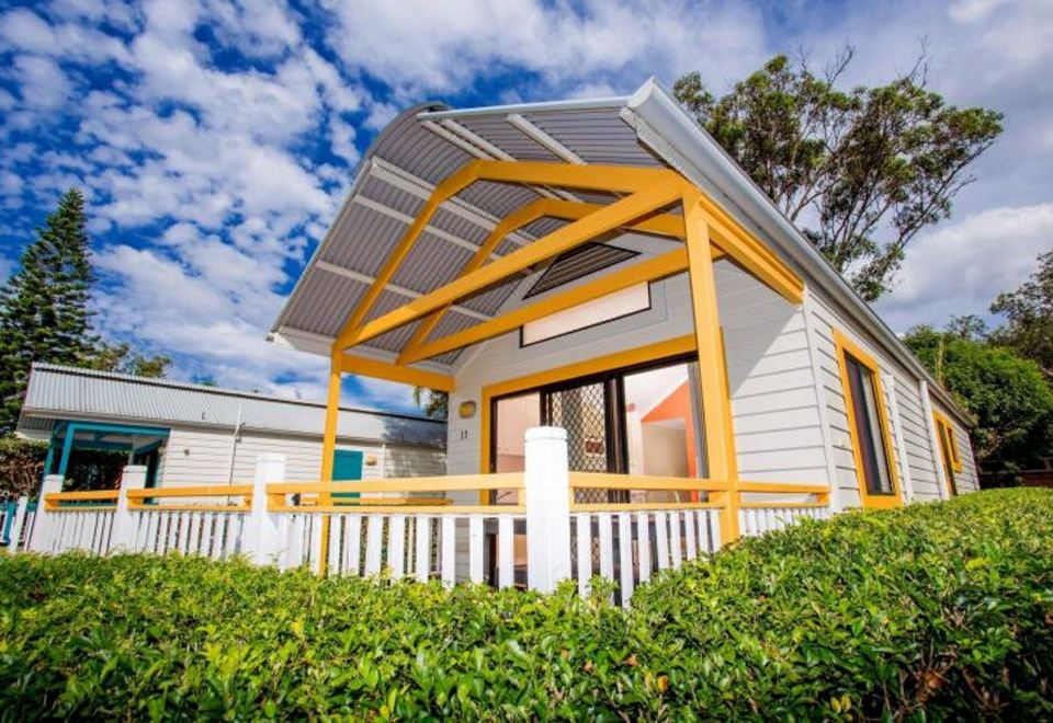 a small yellow and white house with a metal roof , surrounded by bushes and trees at Ingenia Holidays South West Rocks