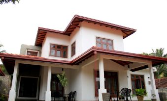 a white two - story house with red trim , situated on a grassy lawn with several chairs placed in front of it at Seasons Villa