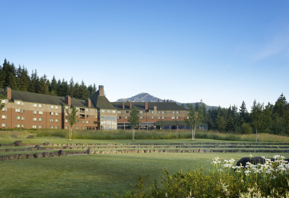 a large brick building surrounded by grass and trees , with a mountainous landscape in the background at Skamania Lodge