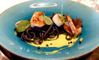 a blue plate with a plate of spaghetti , shrimp , and a sauce is presented on a table at Fletcher Hotel-Restaurant Zevenbergen-Moerdijk